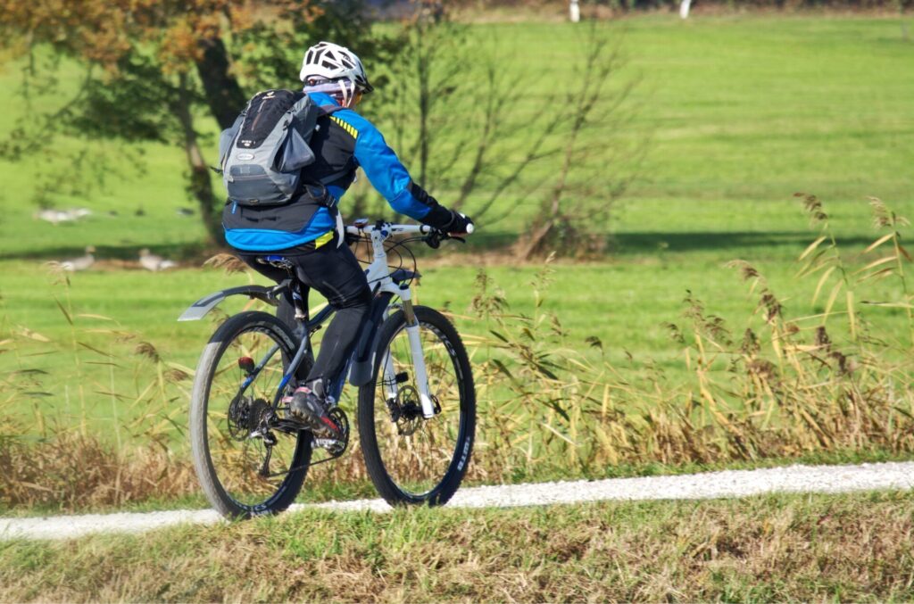 sportlicher Radfahrer mit Rucksack und Helm fährt auf einem Radweg in der Natur